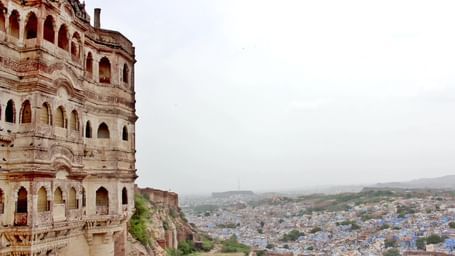 A large historic Indian building with multiple windows overlooking the hazy blue city of Jodhpur, Rajasthan.