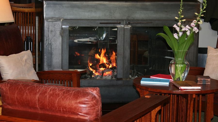 Close-up of a fireplace with a crackling fire, red leather couch, and a small table with books - Brewery Gulch Inn & Spa