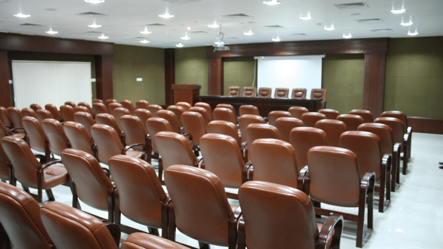 Deva I Hall at DSF Grand Plaza, Tuticorin set up theatre-style with rows of brown leather chairs, a 6-seat head table, and a lowered projector screen.
