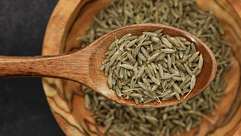 Wooden spoon with brown cumin seeds, inside a wooden bowl, dark background, detailed spice texture.