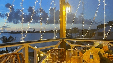 An outdoor dining table set under warm string lights at night, surrounded by tropical flowers and glowing lanterns | Abaco Inn