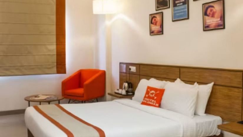 An overview of a room with a double bed and a red single seater sofa inside one of the rooms - Max Hotel Prayagraj