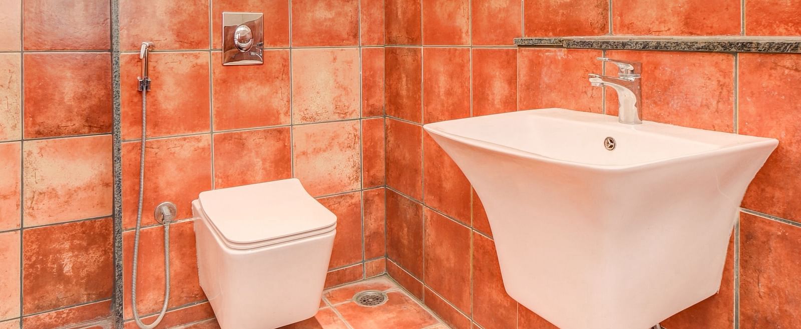 A washroom at Harigovinda's JNStay, featuring a western toilet at the far end and a wash basin to the side