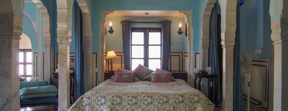 A bedroom at Royal Heritage Haveli featuring a large bed with a patterned cover, blue walls, and arched architectural details.