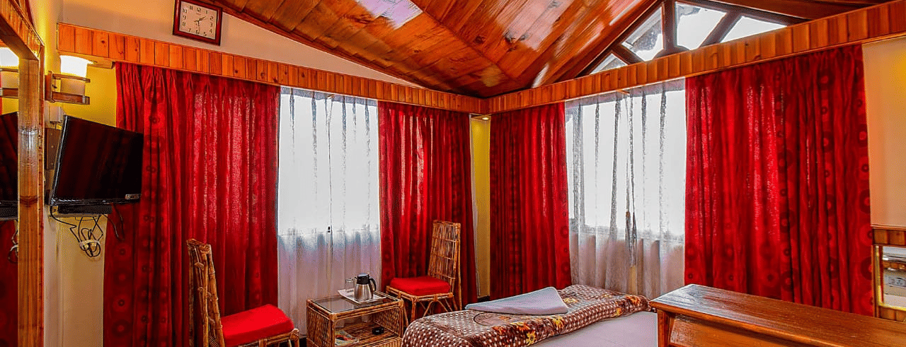 Hotel room with a wooden vaulted ceiling, a double bed, red curtains, and a wall-mounted television at Hotel Dolphin Darjeeling.