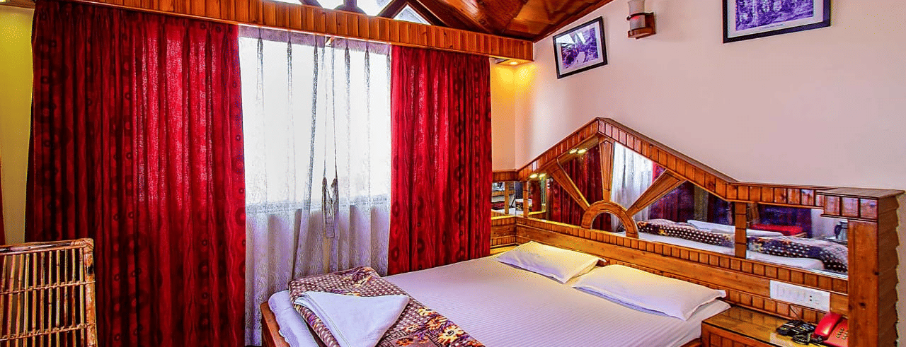 Room featuring a wooden vaulted ceiling, double bed, red curtains, and a wooden dressing table with a large mirror at Hotel Dolphin Darjeeling.