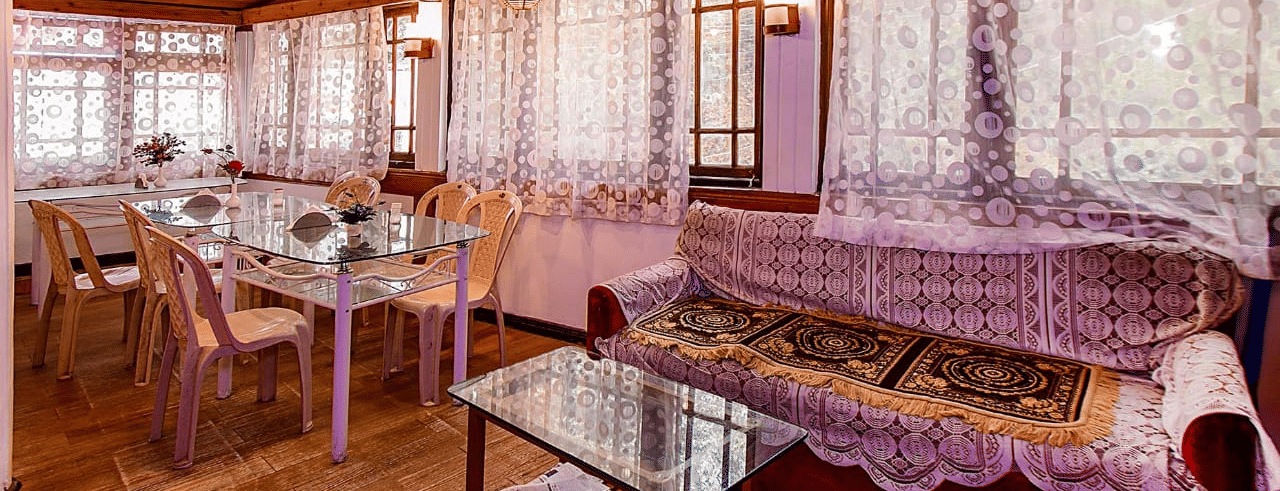 Restaurant/dining room with lace curtains, wooden walls and ceiling, glass tables, and light-coloured chairs at Hotel Dolphin Darjeeling.