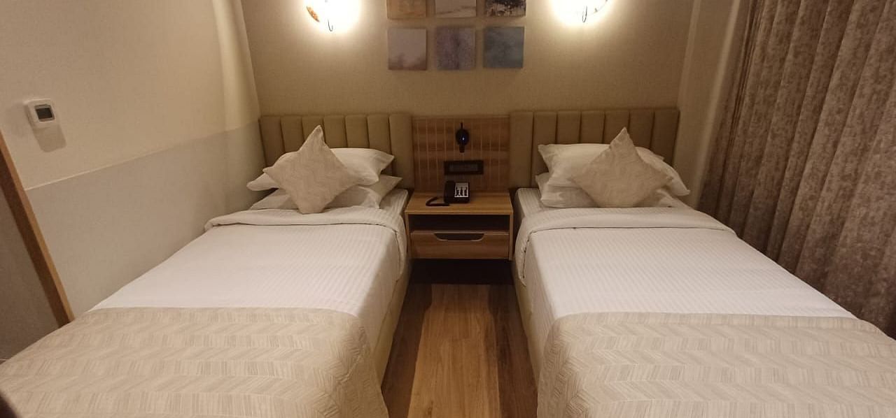 Image of a room with twin beds and a lights above the bed  at Hotel Raai, Hosur.