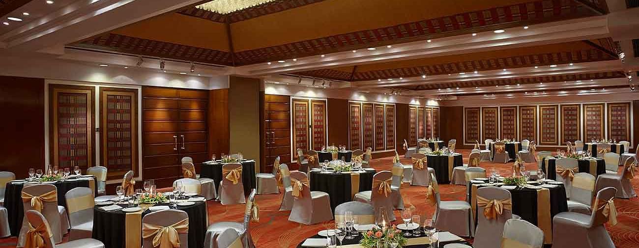 An elegant banquet hall with round tables and chairs adorned with decorative sashes, perfect for hosting formal events and celebrations.