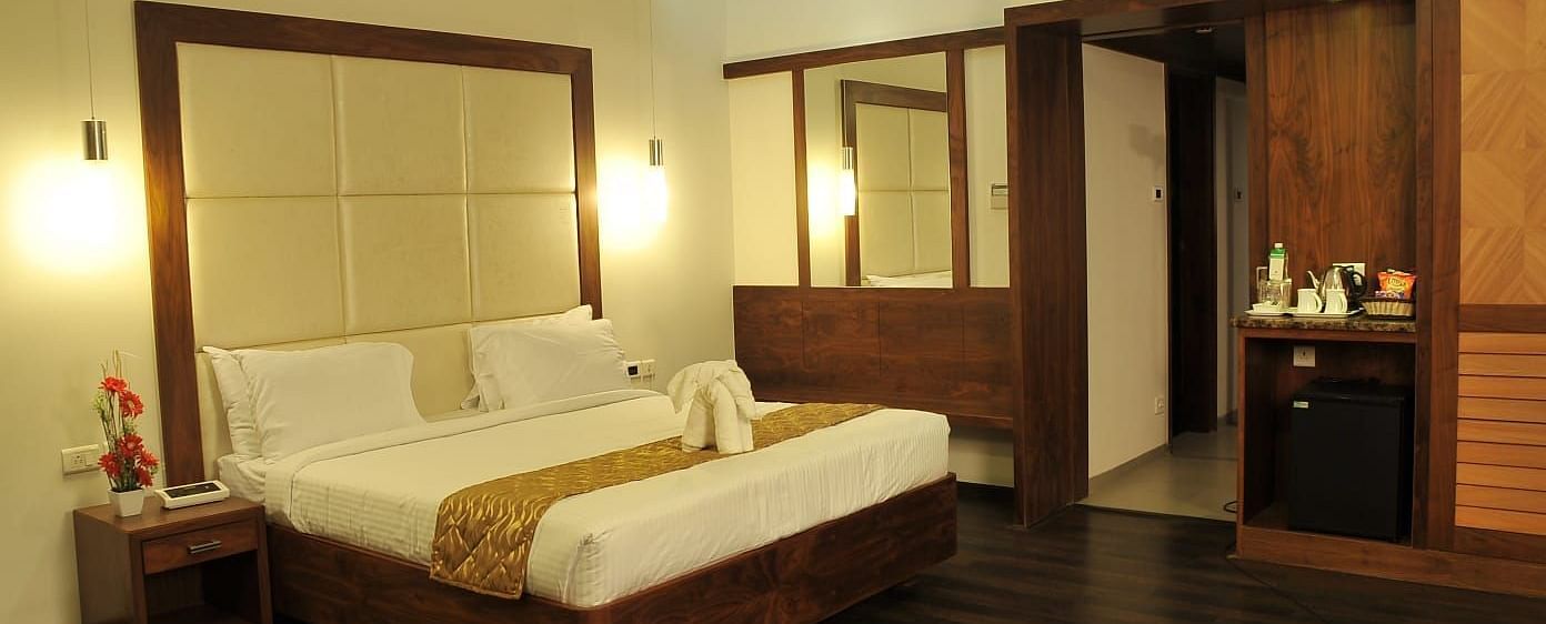 A Executive Suite at Dhanalakshmi Srinivasan Hotels, Perambalur featuring a bed with white linens, dark wood flooring, and a mini-fridge.