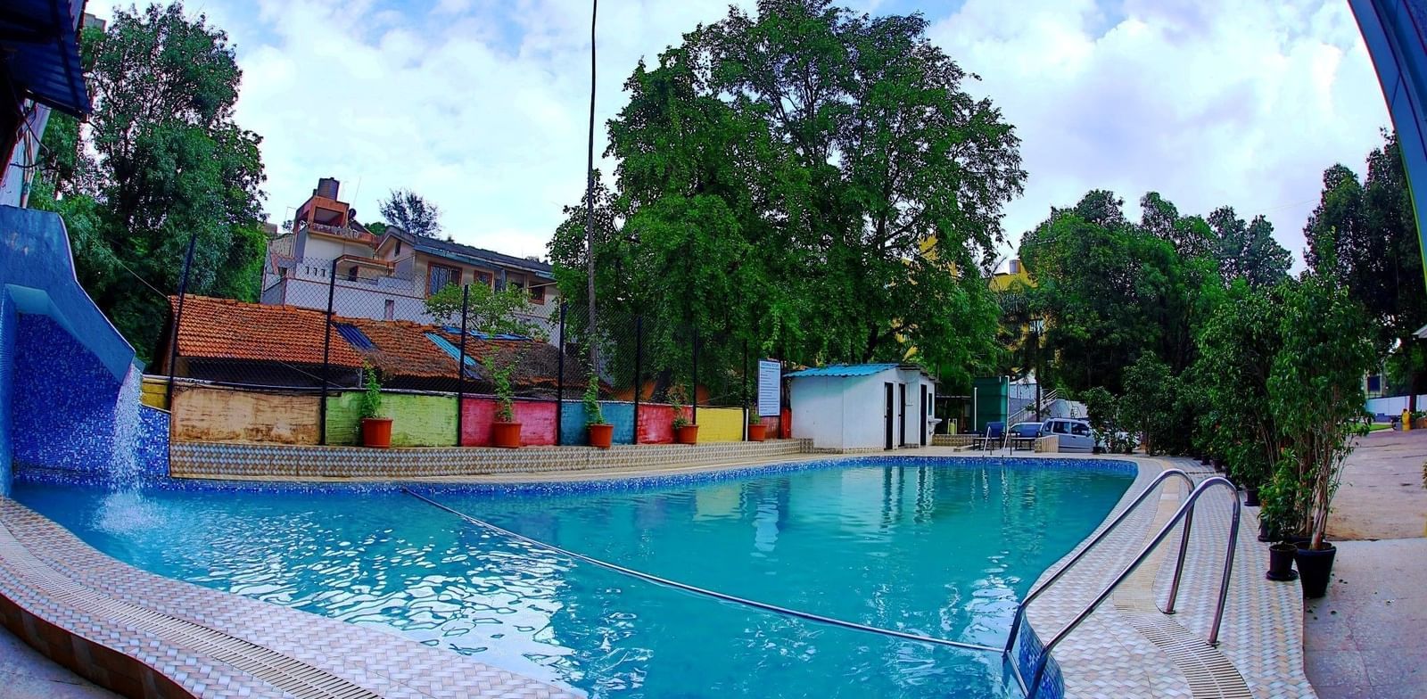 Assymetrical large swimming pool at Krushnai Resort under a partly cloudy blue sky.