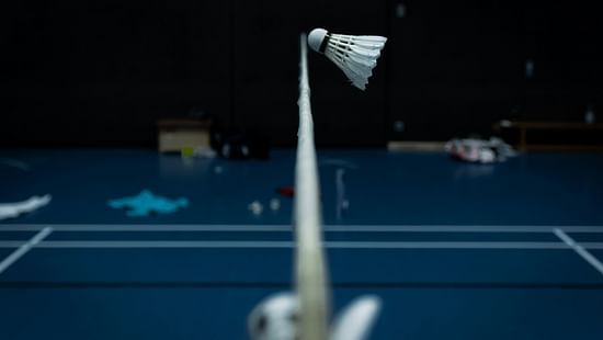 An overview of a badminton court with a cock flying just above the net