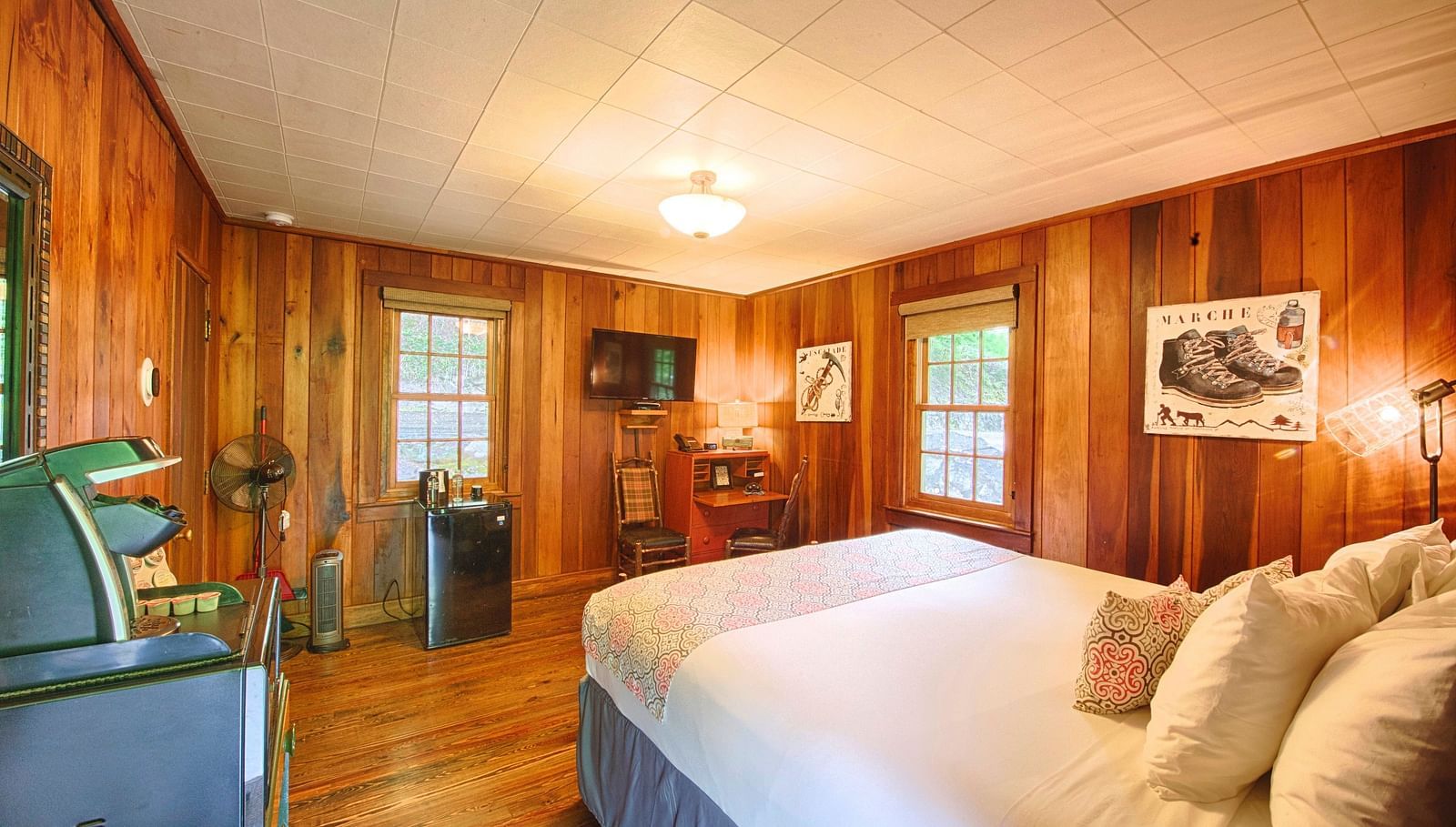 a bedroom with wooden interiors with two windows and a wall mounted television placed opposite to the double bed - Historic Tapoco Lodge