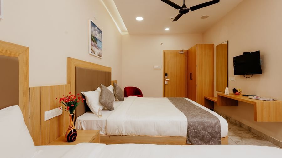 A well-furnished bedroom at Daksh The Grand Gowardhan, Dwarka, featuring comfortable beds and a wall mounted flat-screen television.