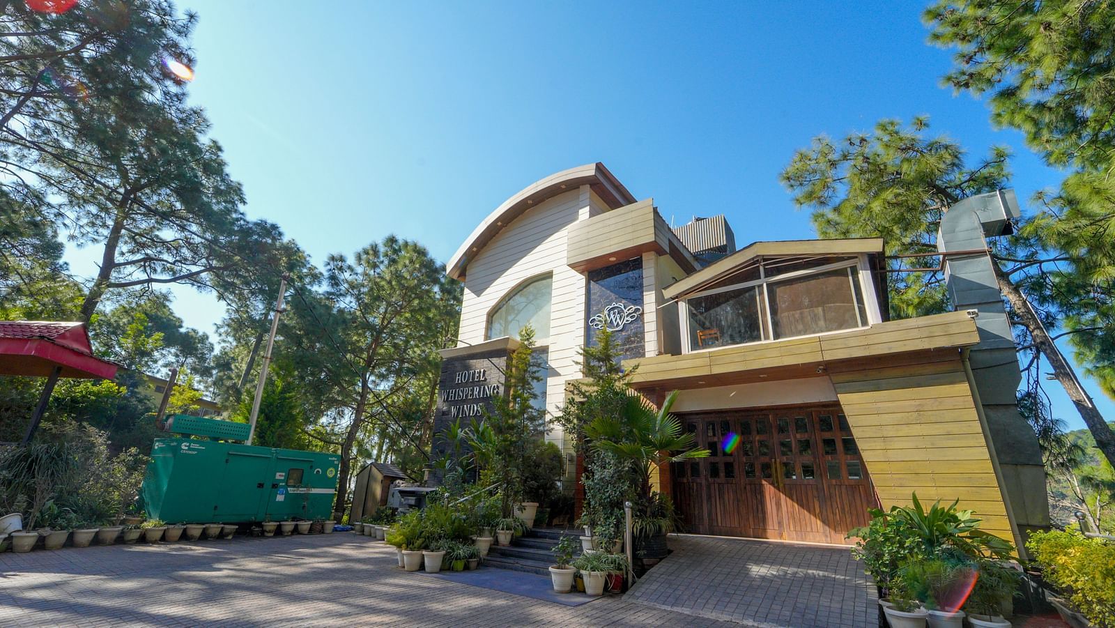 A facade shot of DLS Whsipering Winds taken from an angle showing the hotel building amidst trees with a clear sky in the background