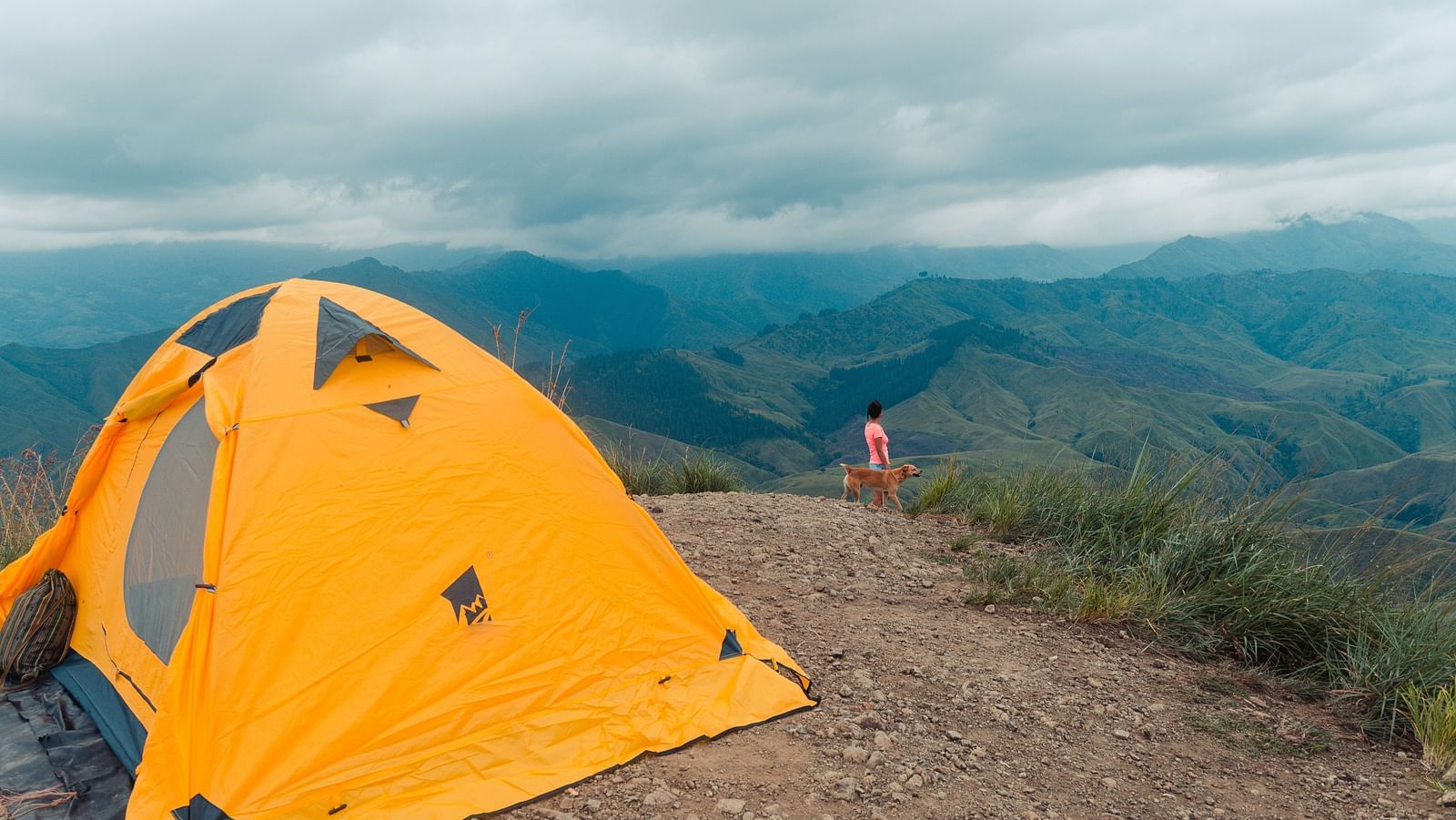 Yellow camping tent on a hill with white clouds in the background