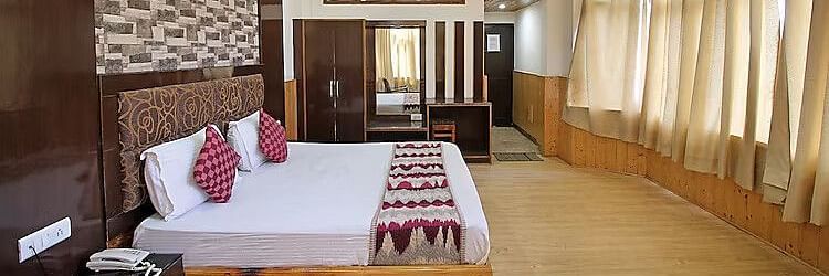 A view of a room at DLS Hotel Devlok, Manali with a double bed, side tables, a wardrobe with a mirror and  large windows