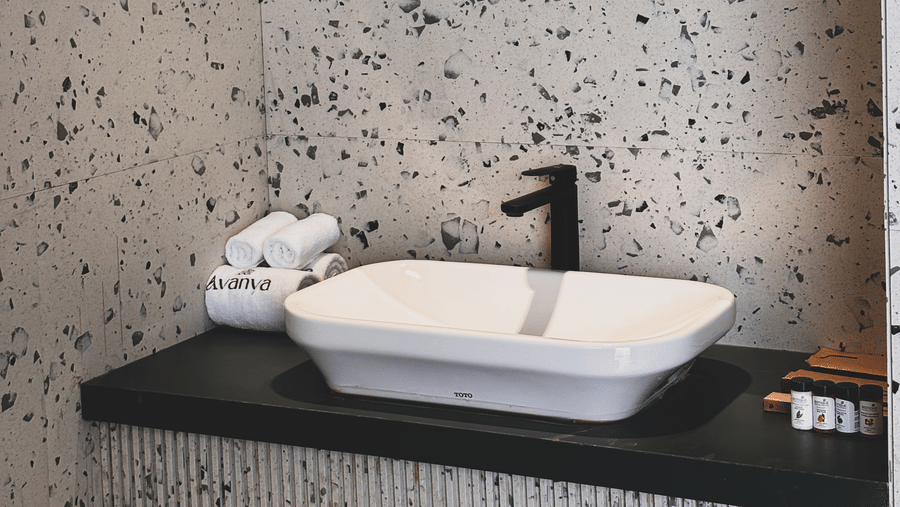 A white rectangular washbasin with a black tap is mounted on a black counter against terrazzo walls at Avanya Resorts N Retreat.