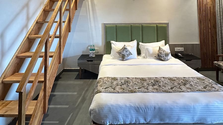 A spacious hotel room with a king size bed, a wooden ceiling, and a loft area accessible by a staircase.