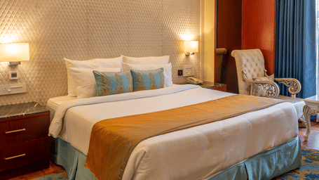 Luxurious bedroom with exposed dark wooden ceiling beams, a large bed, and intricate textured wall behind the headboard at Hotel Hukam's Lalit Mahal.