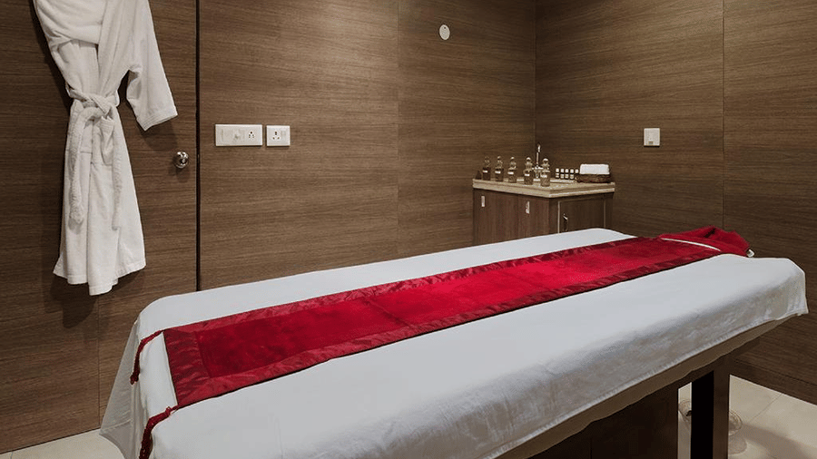 A massage table topped with white and red linens stands near a hanging bathrobe at Ramada by Wyndham Mussoorie Mall Road.