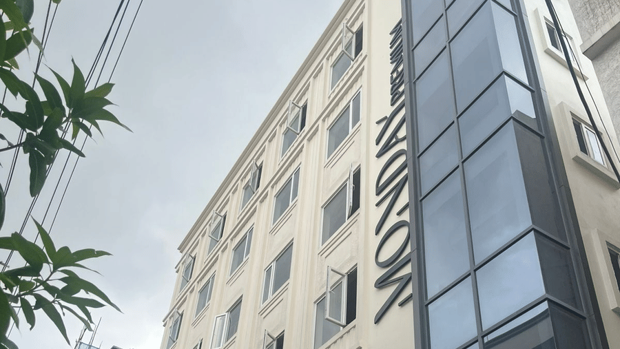  Contemporary exterior view of Monday Premium, Madhapur, showing a multi-storey building with a glass-fronted stairwell and a cream-coloured facade. 