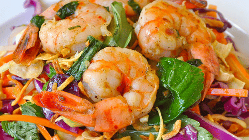 A plate of shrimp salad with vegetables including cabbage, carrots, and onions arranged on a white dish.