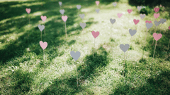 Heart-shaped signs on thin sticks are placed across a green grass lawn under natural sunlight.