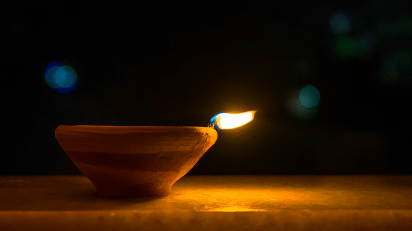 A close up of a lit deepam in a clay pot with the background blurred.