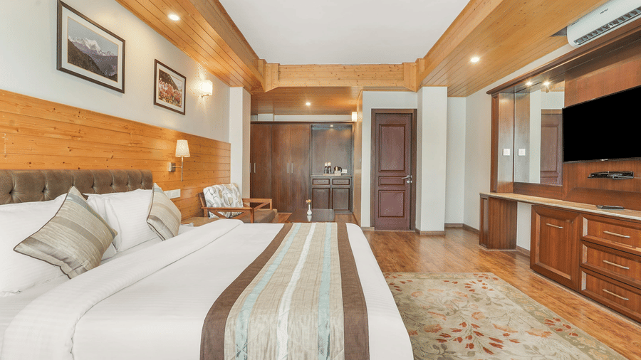 A large bedroom with wooden ceilings and flooring, featuring a bed, a television console, and framed artwork on the wall.