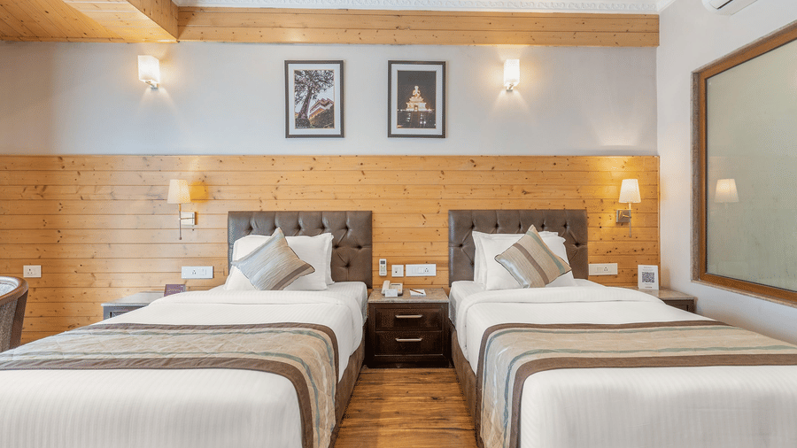 A hotel room configured with two separate single beds, wooden headboard panelling, and symmetrical bedside lamps.