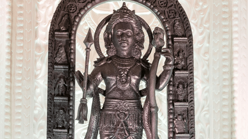 A carved wooden statue of a multi-armed deity stands inside a temple archway.