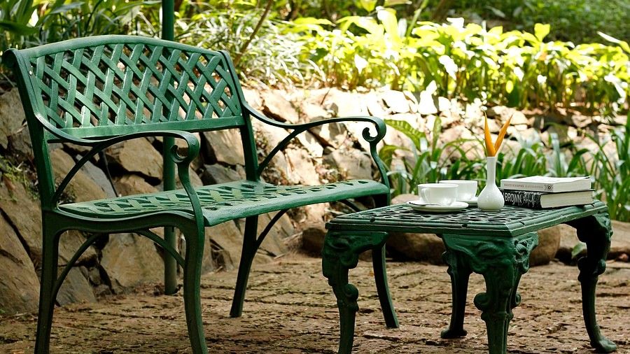 A green garden bench and table set with a teacup, saucer, and book on top.