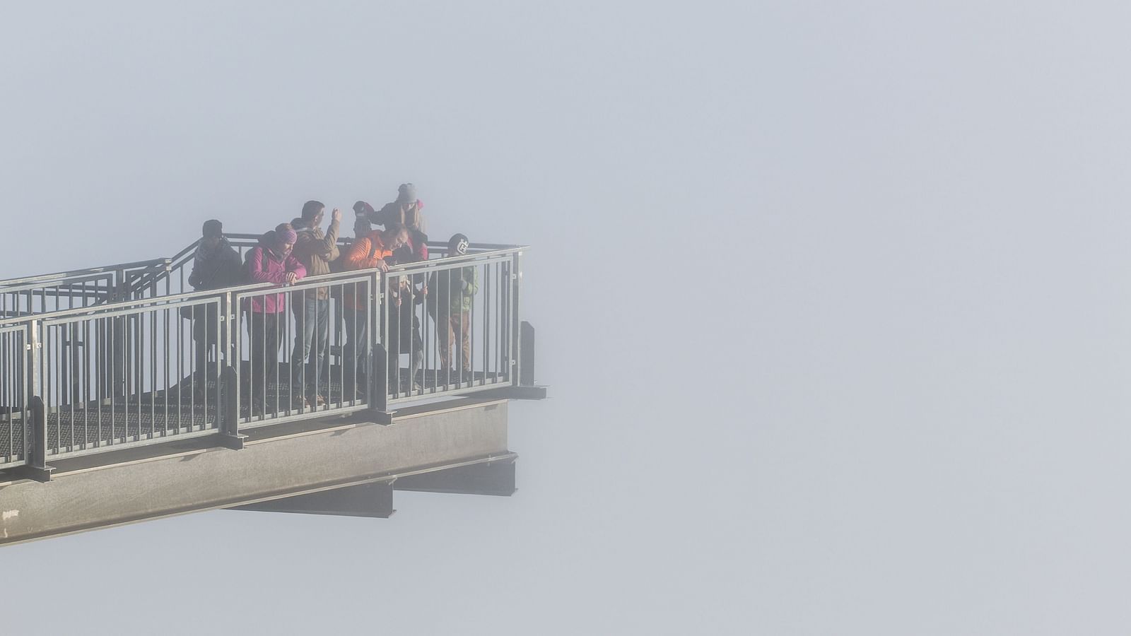 A group of people looking below while standing in a skywalk.