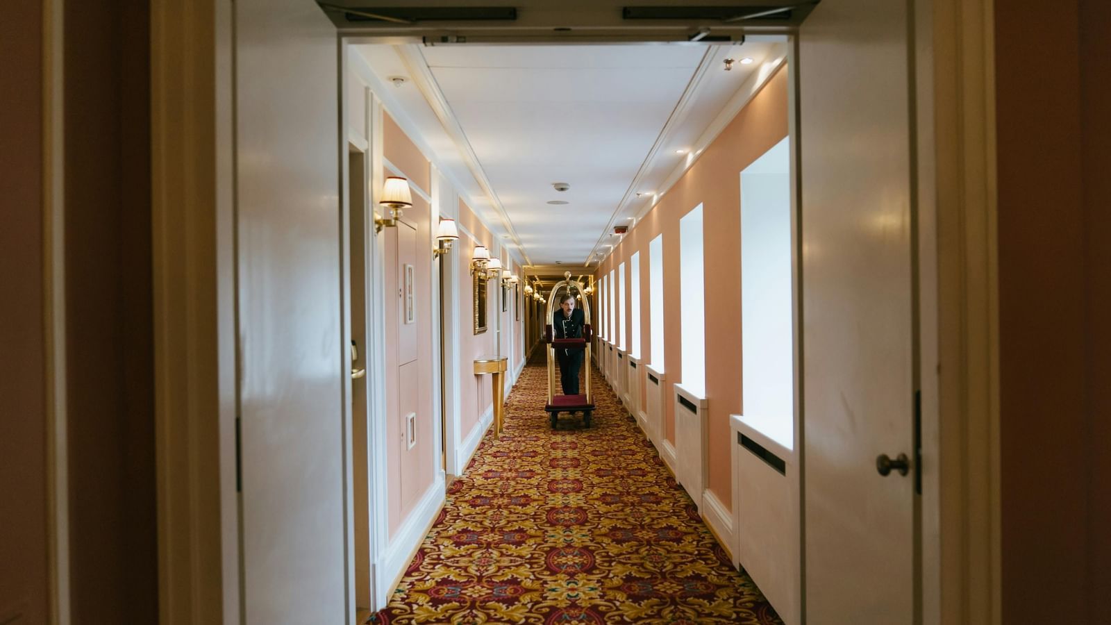 A hotel room hallway and a butler pushing a cart with luxurious decor, carpet and windows