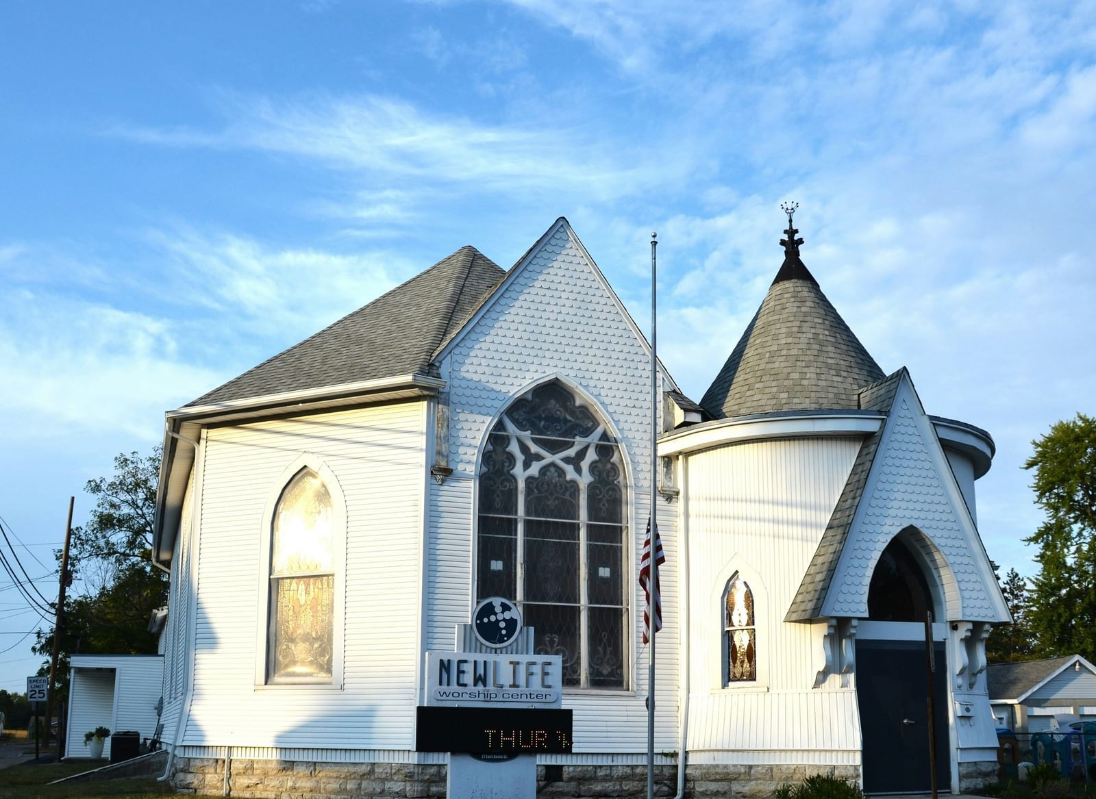 A white church with a steeply pitched roof and tall, arched windows against a bright blue, cloudy sky.
