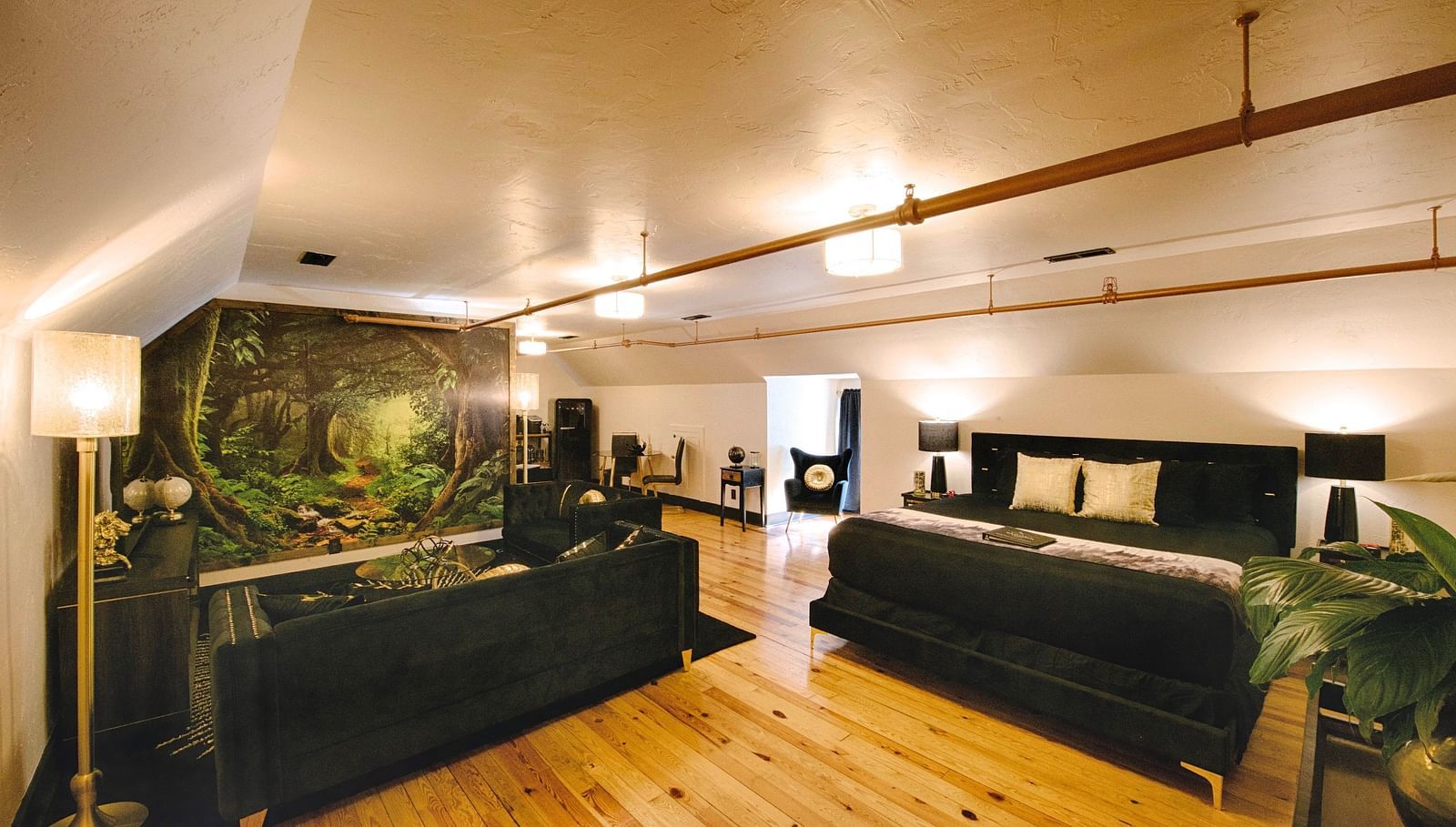 a spacious bedroom with a cozy double bed and black couch set in the common seating area with a jungle mastiff made in the feature wall of the suite - Historic Tapoco Lodge