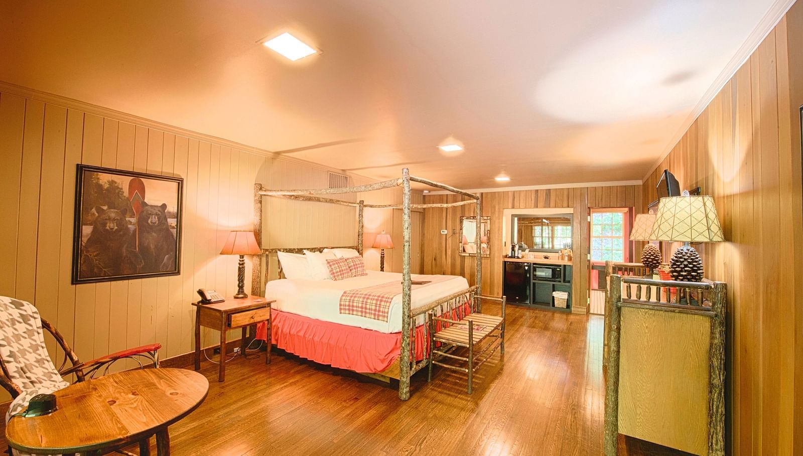 a bedroom with cozy interiors and wooden flooring featuring a double bed along with seating area with a round coffee table - Historic Tapoco Lodge
