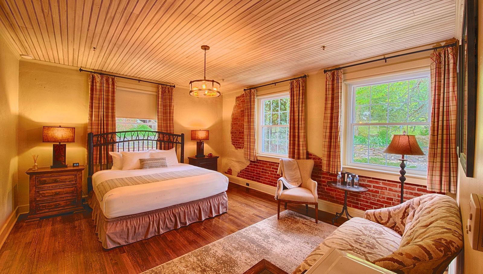 a room with ample natural lighting coming from the huge windows in the room with plush arm chairsa brightly lit bathroom featuring a door opening to the bedroom overlooking the double bed - Historic Tapoco Lodge