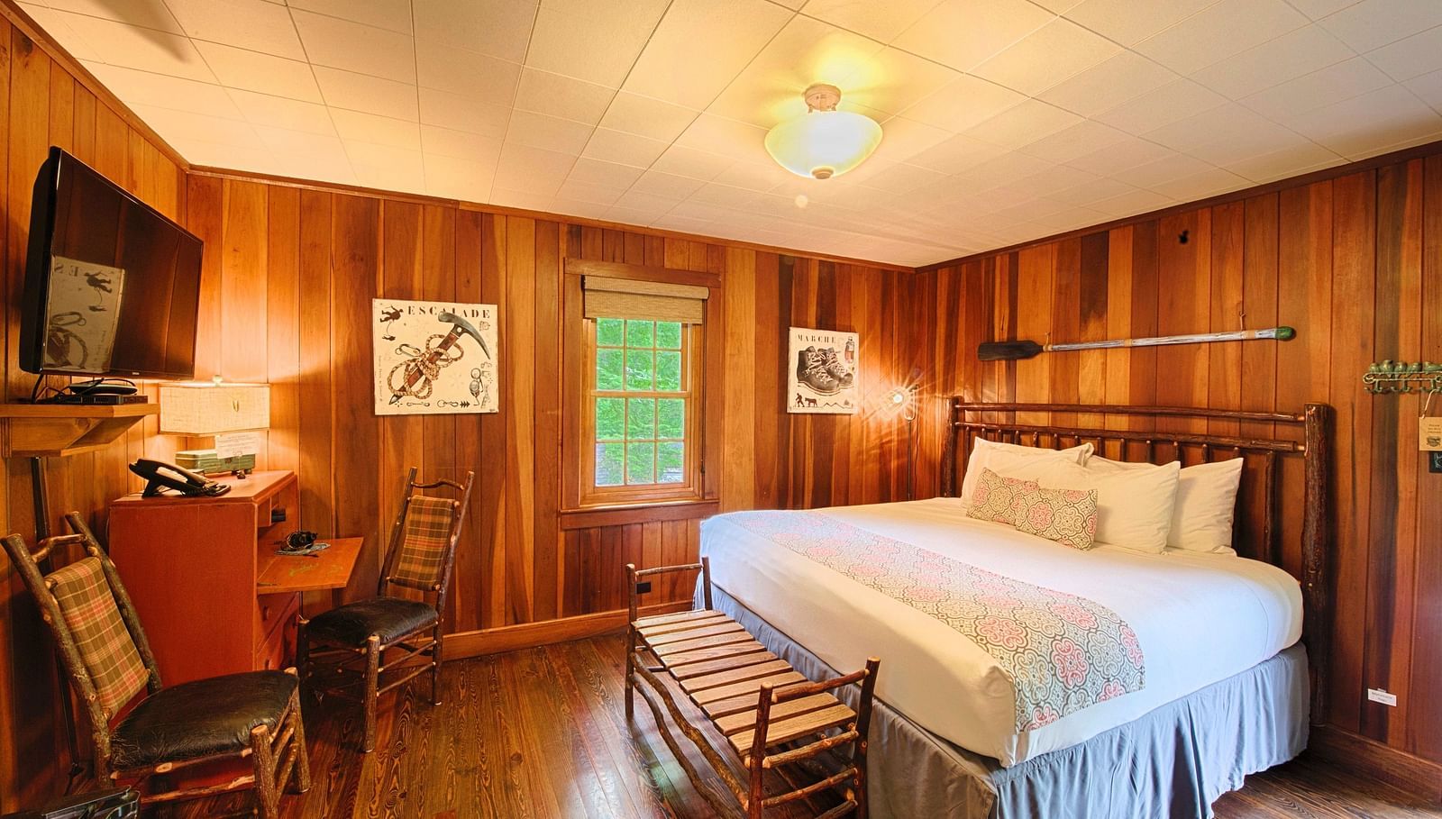 a room with wooden walls featuring a double bed with soft pillows arranged over it along with a wall mounted television right in front of it - Historic Tapoco Lodge
