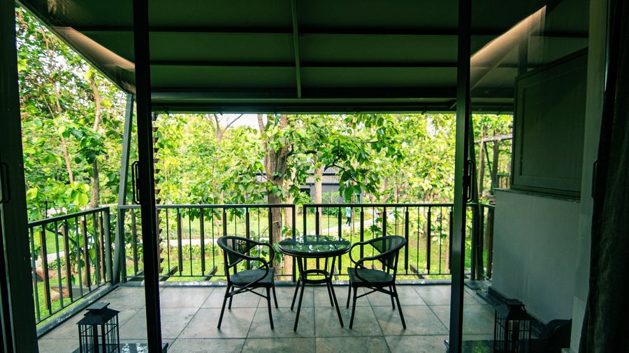 A balcony with two chairs and a table neatly arranged, overlooking the lush greenery at Hotel Sonar Bangla Joypur Forest, Bankura.