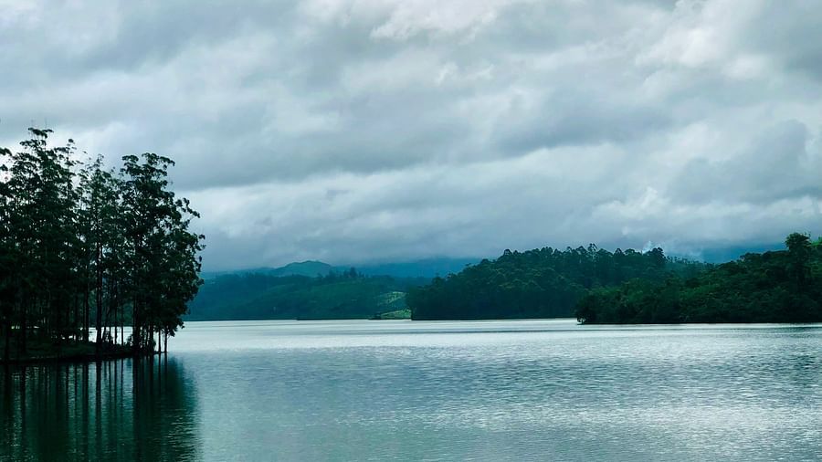 An overview of a lake in Valparai with trees on the land and dark clouds above