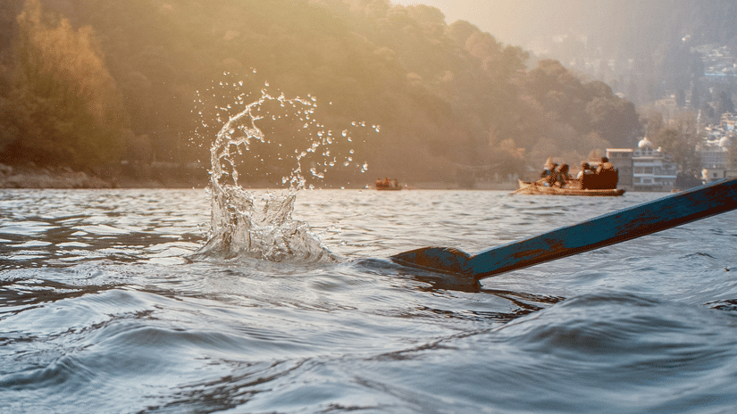 A person paddling on the Ganges at sunrise with misty hills in the background.