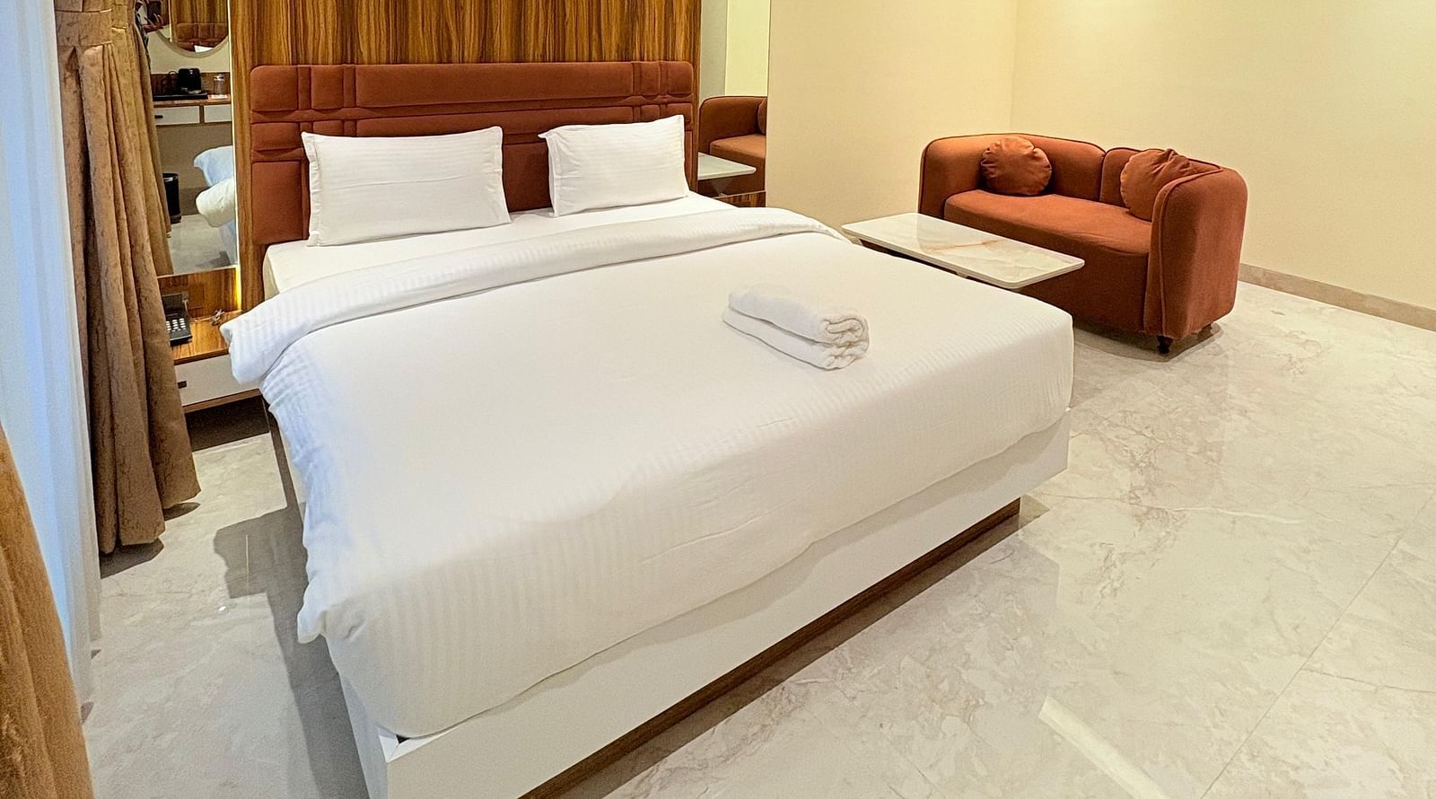 Spacious bedroom with a bed and a sofa placed next to it, offering a seating area at Hotel Mumbai House, Vashi.