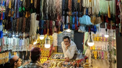 People are browsing through various items hanging in a dimly lit market stall or shop.