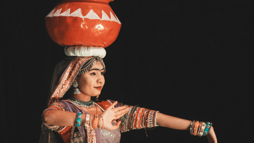 An artist enacting rajasthani folk dance with many pots stacked on top of each other above her head.