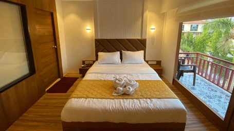 Well-lit luxury room featuring a king size bed and large glass doors leading to a private wooden balcony - DAN Resorts & Weddings, Palghar