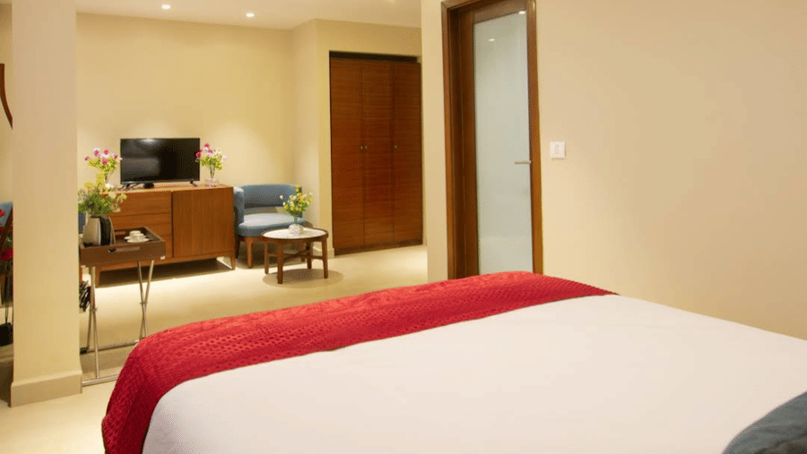 A spacious bedroom with a red runner, wooden accents, television, and blue chair at Estherea Elite, Morjim.