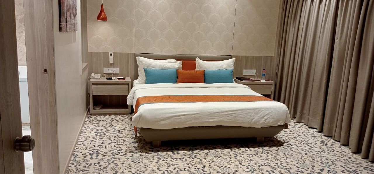 A contemporary hotel bedroom featuring a large bed with white bedding, decorative cushions, and warm ambient lighting.