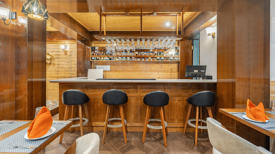 A serene bedroom interior with polished wooden flooring, showing a king-size bed in the foreground and a large window in the background that frames a view of lush green trees.